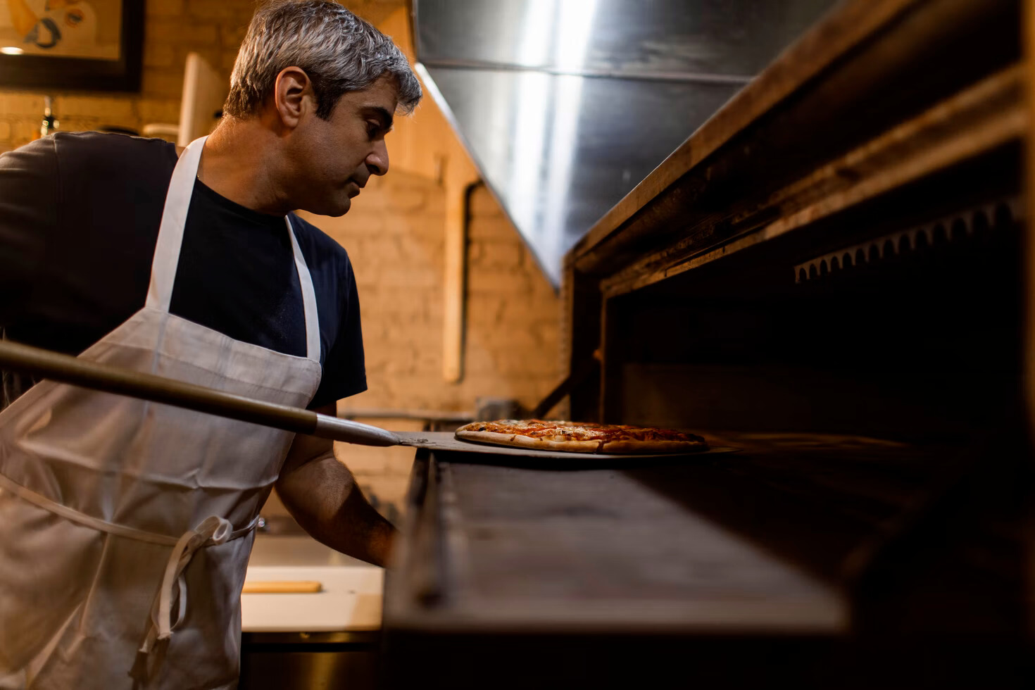 chef putting pizza into oven